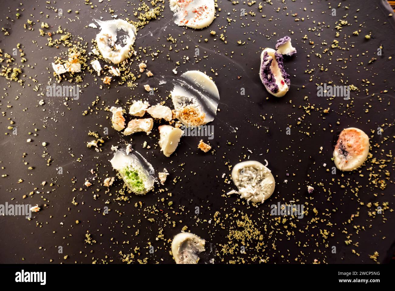 Abstract composition - crumbs of colorful cakes cookies spread over the dark plate background Stock Photo