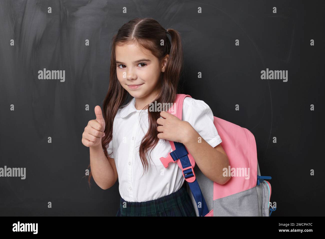 Cute schoolgirl showing thumbs up near chalkboard Stock Photo - Alamy