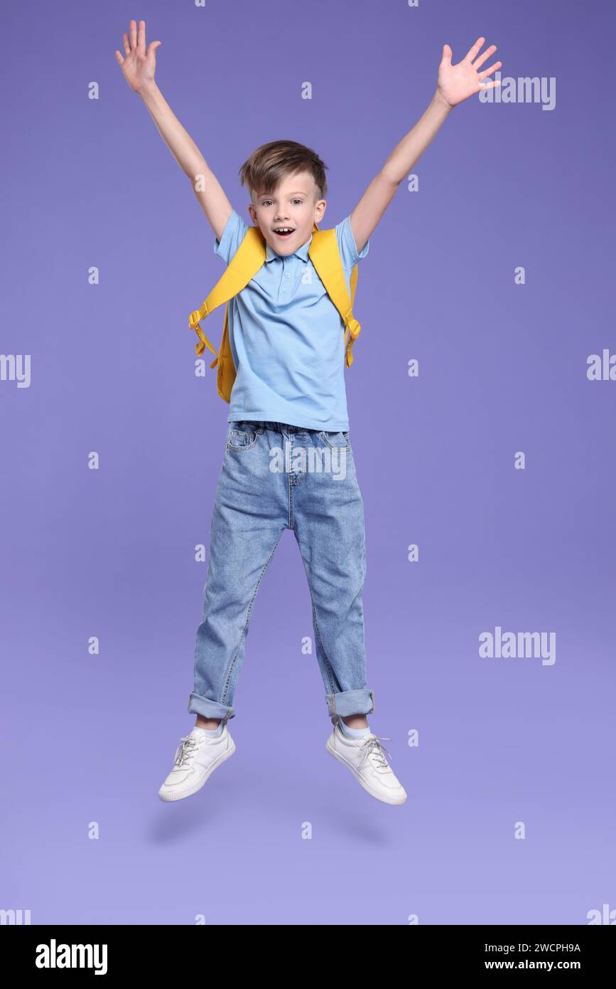 Back to school. Cute boy with backpack jumping on violet background ...