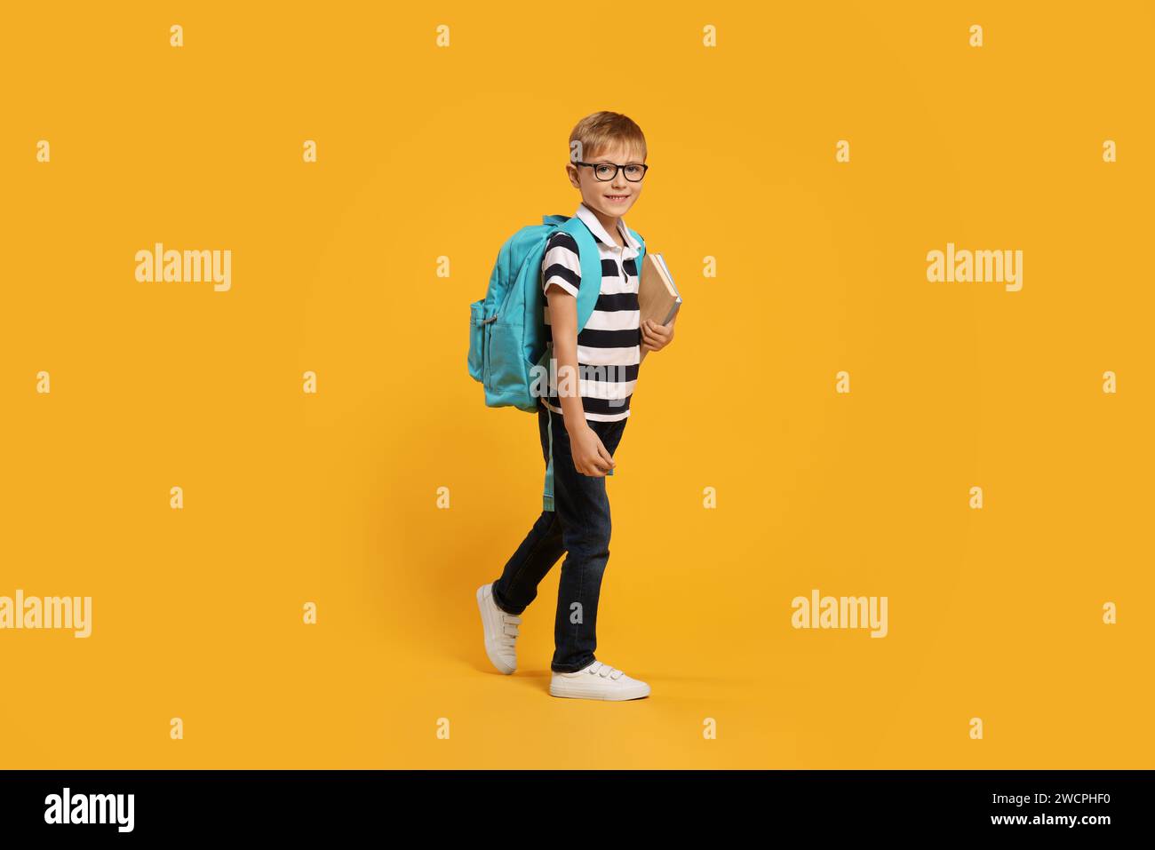 Happy schoolboy in glasses with backpack and books on orange background ...