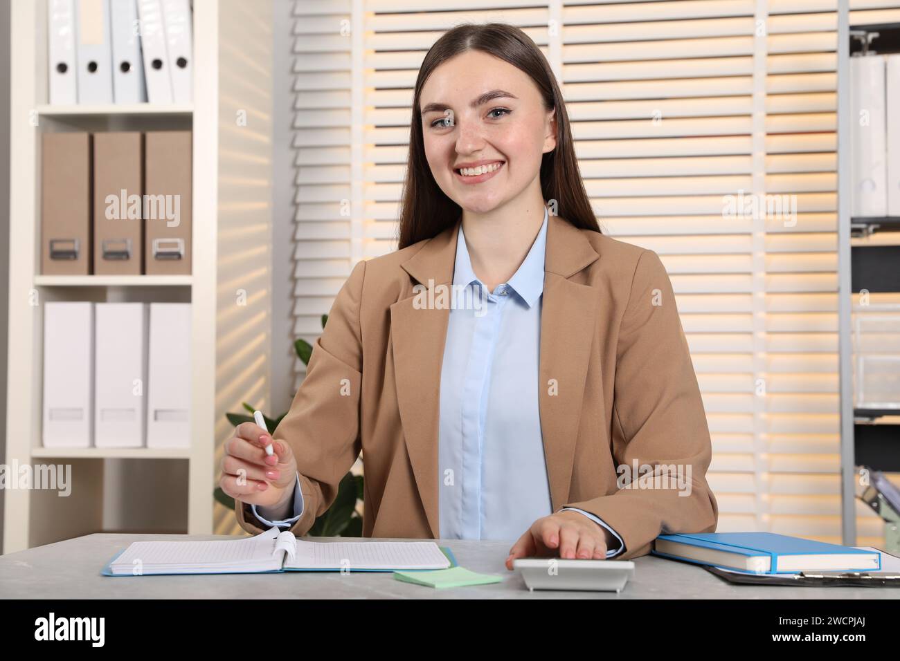 Happy woman taking notes while using calculator at light grey marble table in office Stock Photo