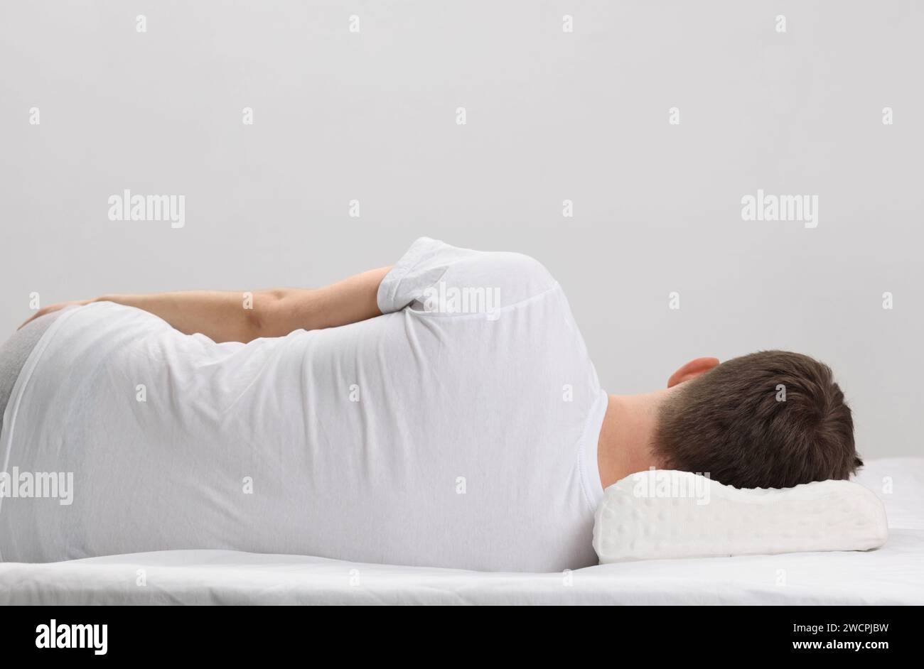 Man sleeping on orthopedic pillow against light grey background Stock