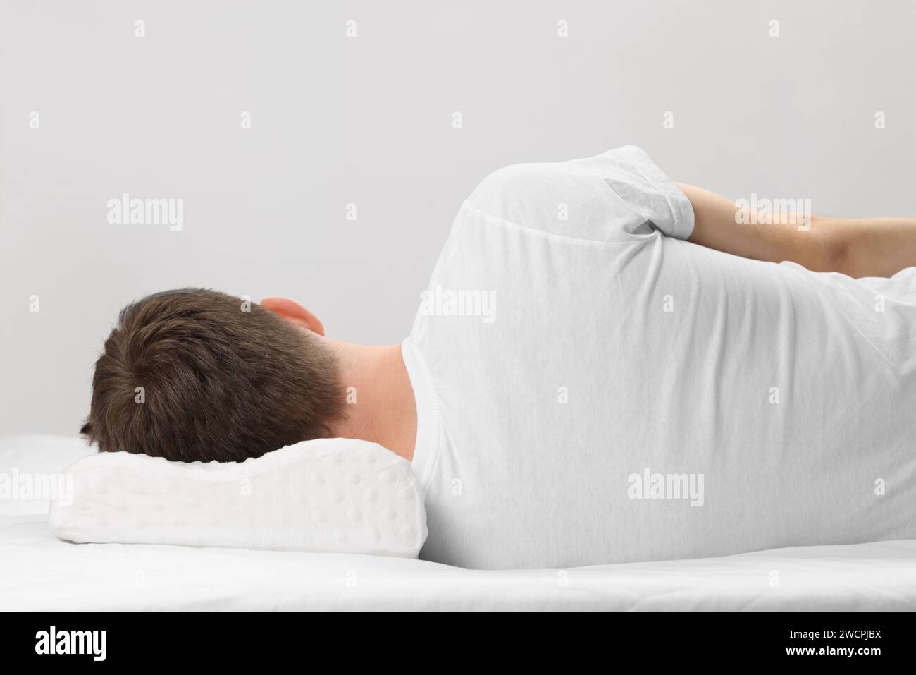 Man sleeping on orthopedic pillow against light grey background Stock