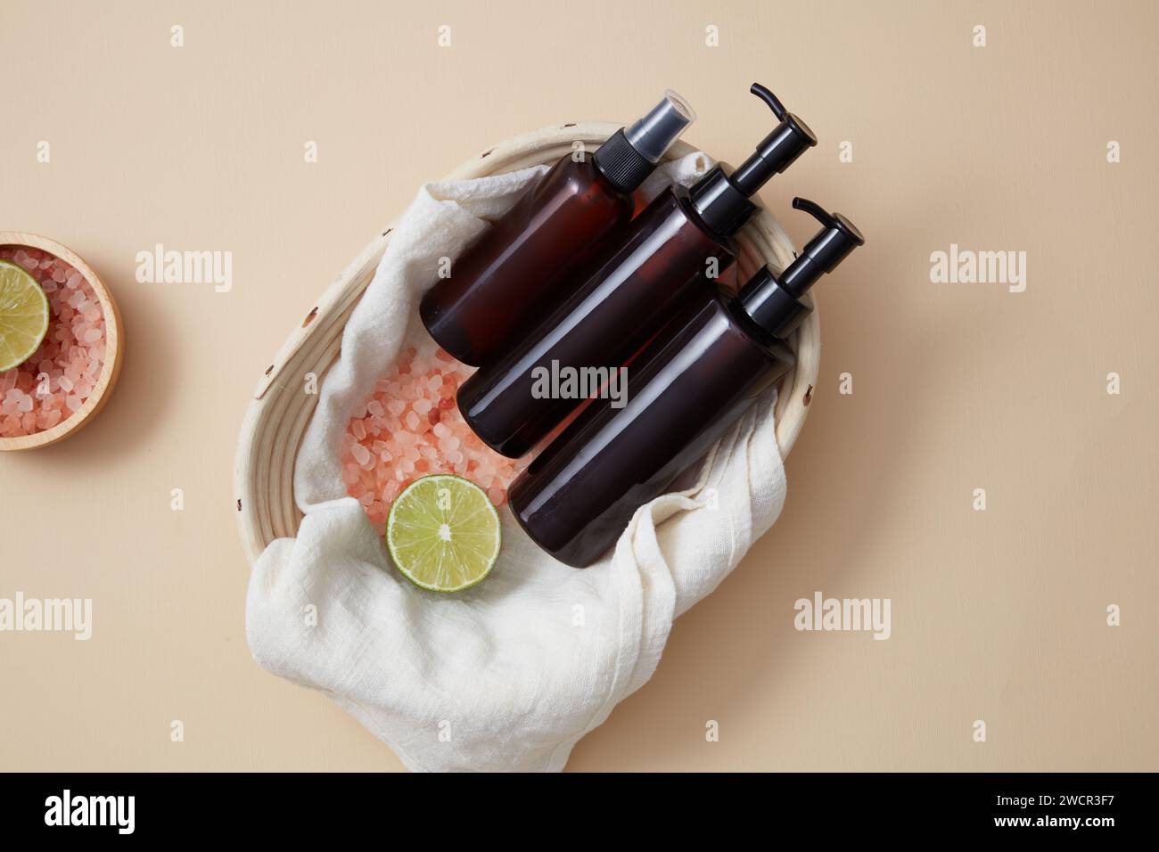 Empty label pump bottles and spray bottle displayed in a basket with a bowl of pink salt and lime slice arranged beside. Shampoo or conditioner hair c Stock Photo