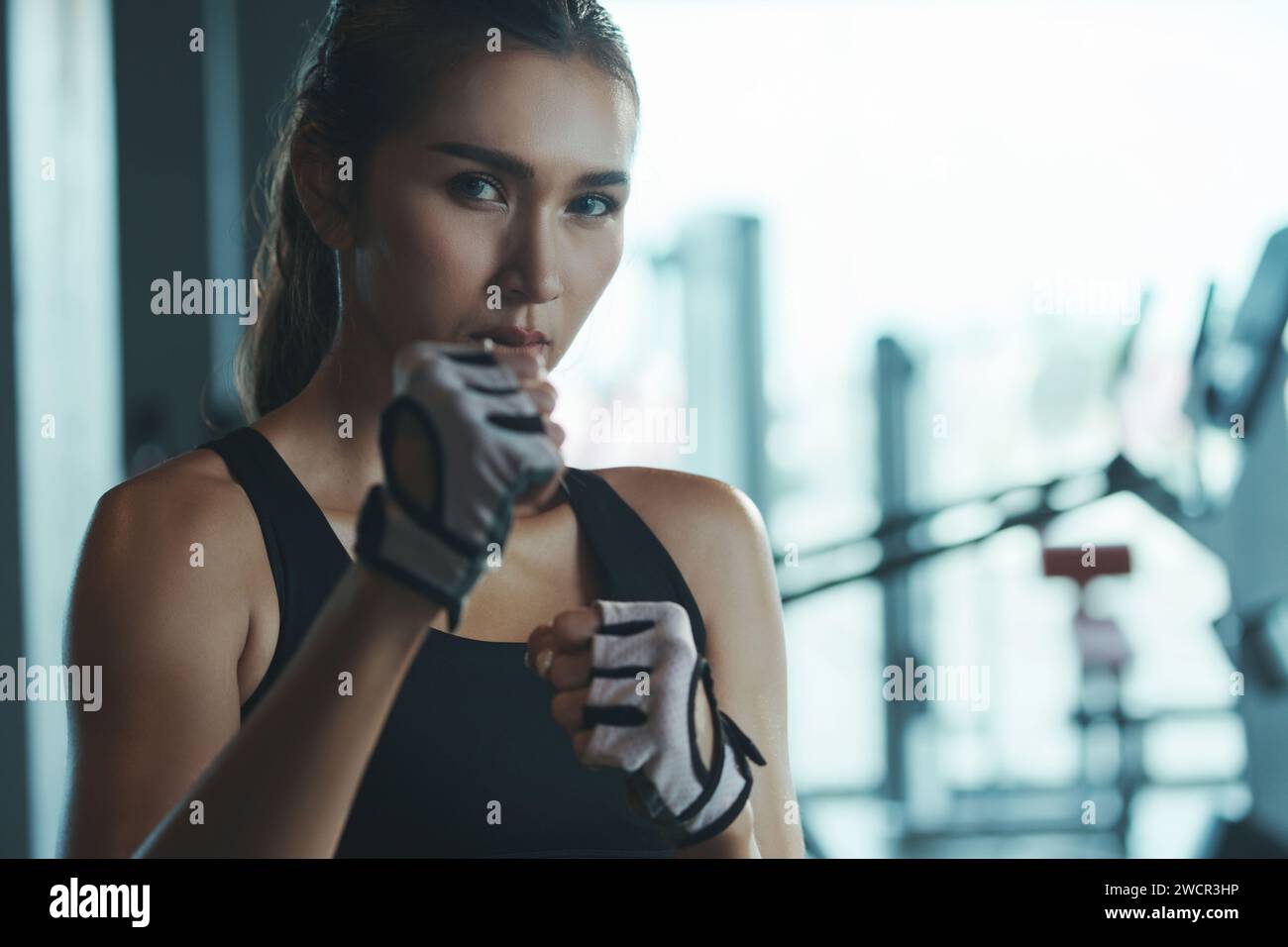 Sporty woman wearing boxing gloves poses in fighting position looking at camera. Stock Photo
