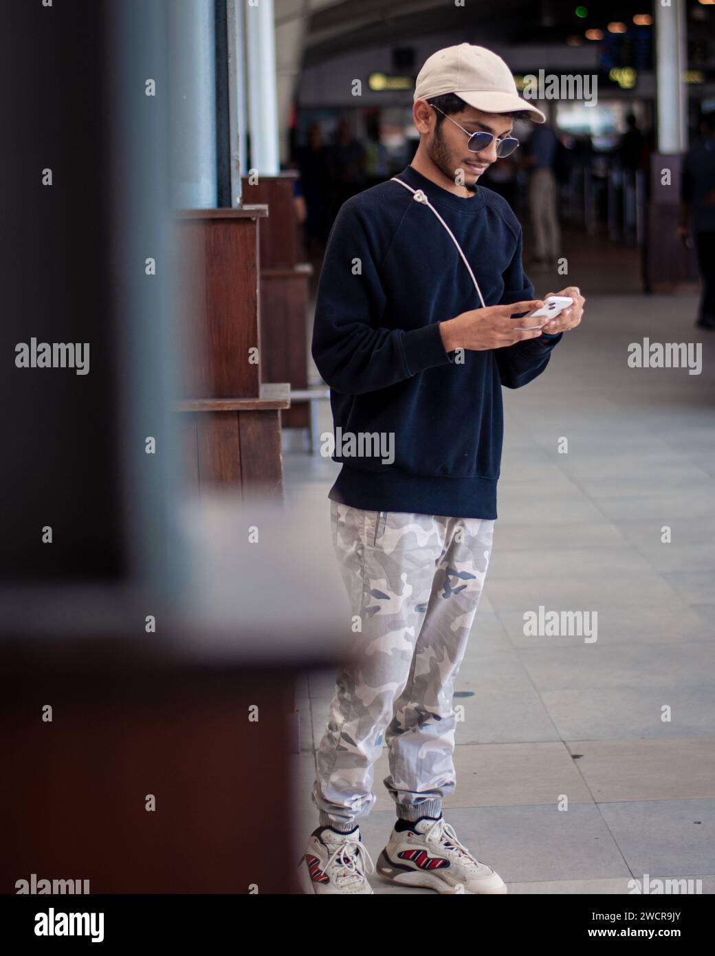 Picture of an Indian guy wearing black dress a cap and shades looking at the phone Stock Photo