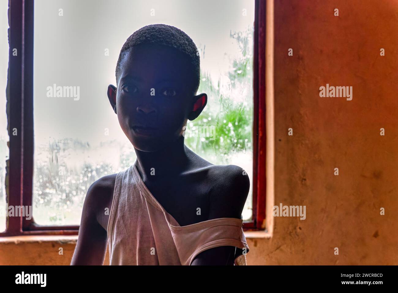 rainy day, girl standing by the window, thin body underweight, poverty in the favela Stock Photo