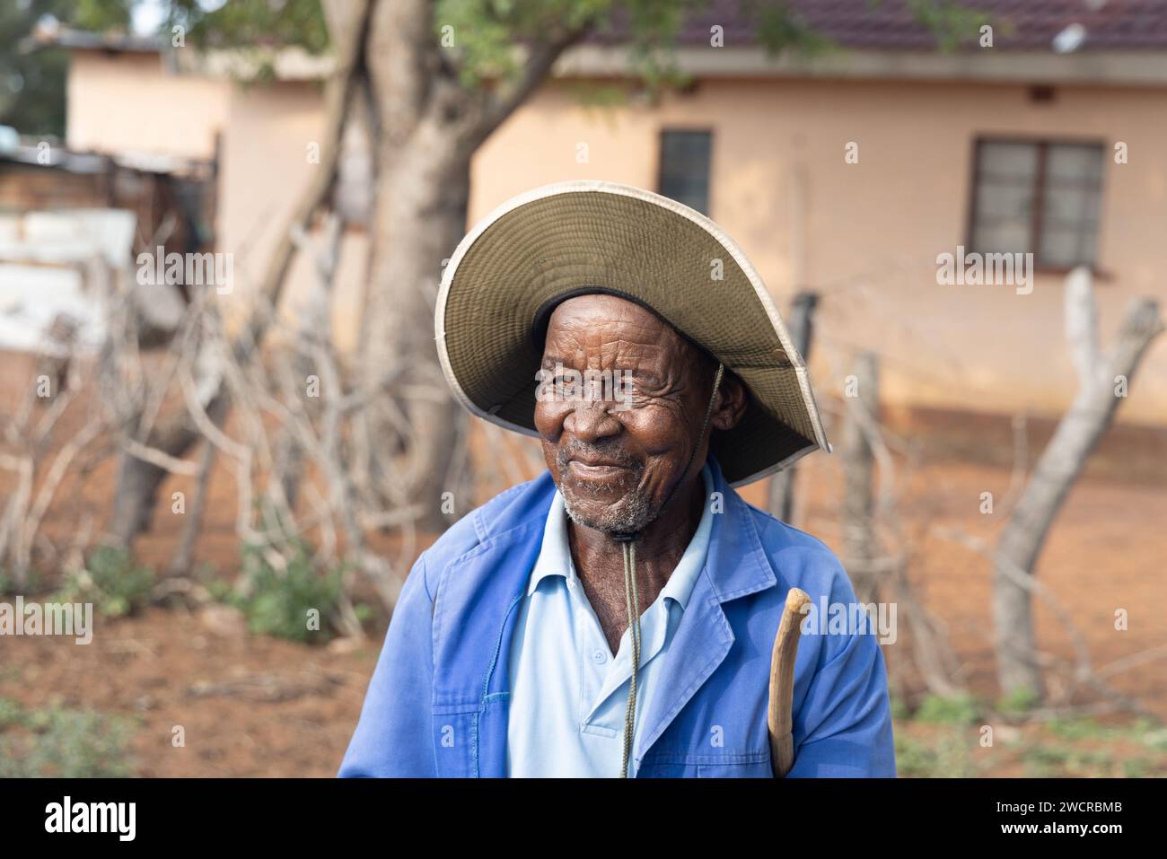 portrait of an old african man with a stick in the village in front of a house Stock Photo