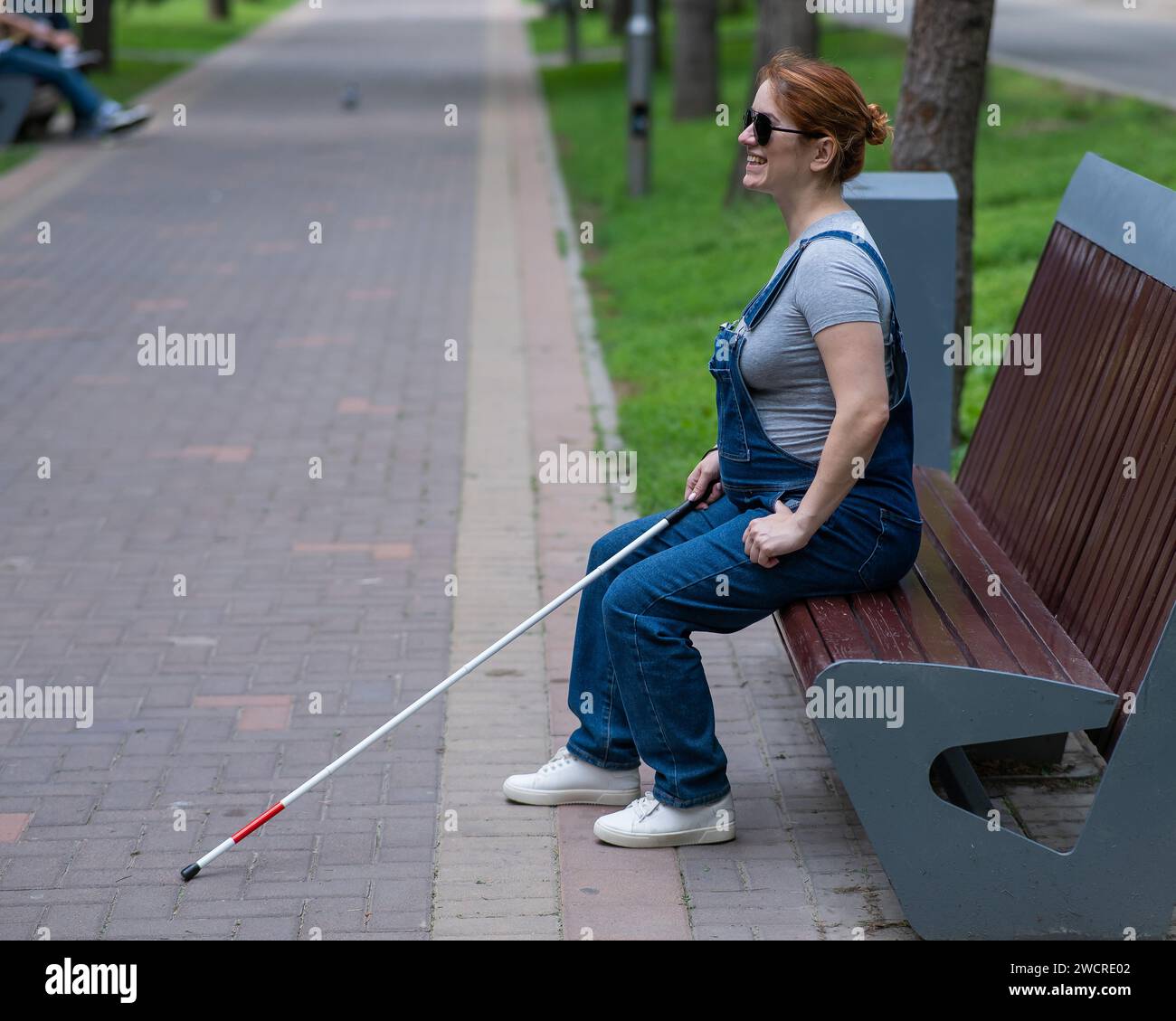 Blind red-haired pregnant woman sitting on a bench outdoors.  Stock Photo