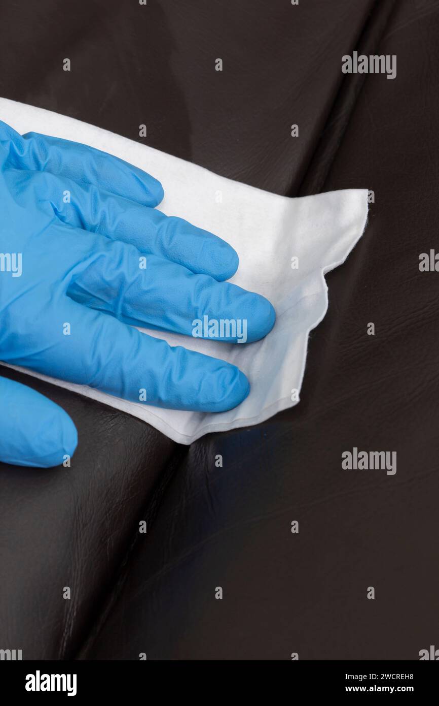 Person cleaning a brown leather sofa couch with a leather cleaner wipe