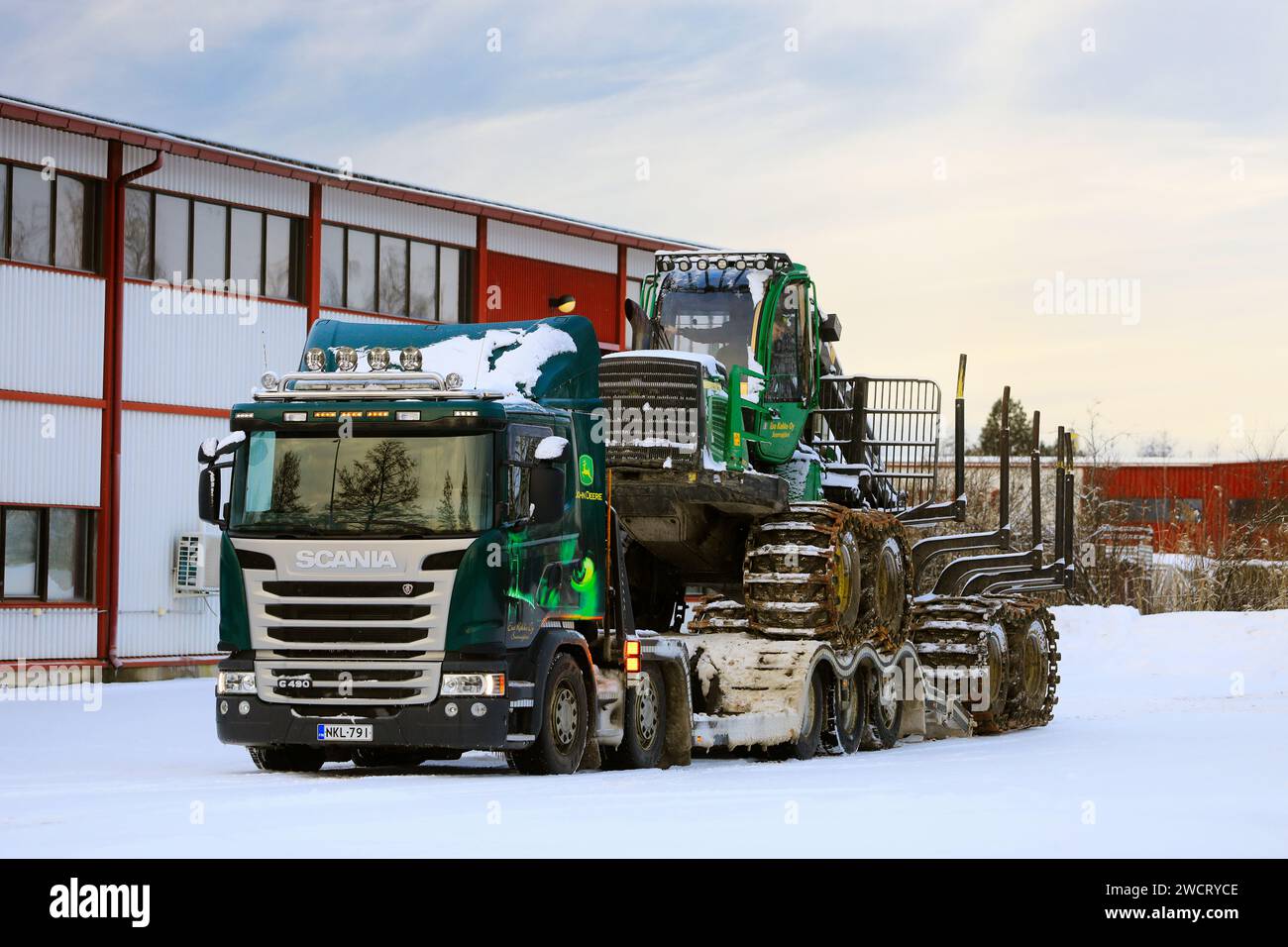 Loading John Deere 1210E forestry forwarder onto Scania G490 truck trailer for transport on a day of winter. Salo, Finland. December 27, 2023. Stock Photo