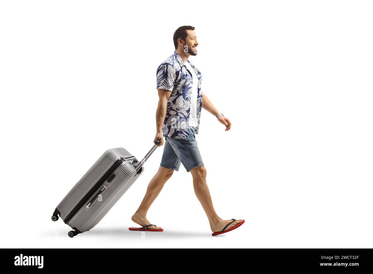 Man in flip-flops pulling a suitcase smiling and walking isolated on white background Stock Photo