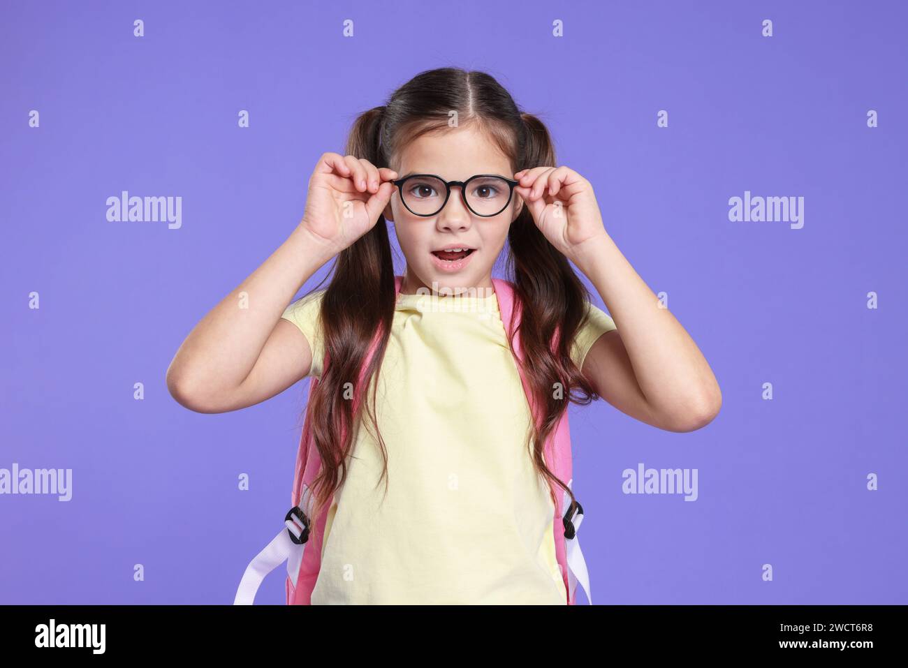 Cute schoolgirl in glasses with backpack on violet background Stock ...