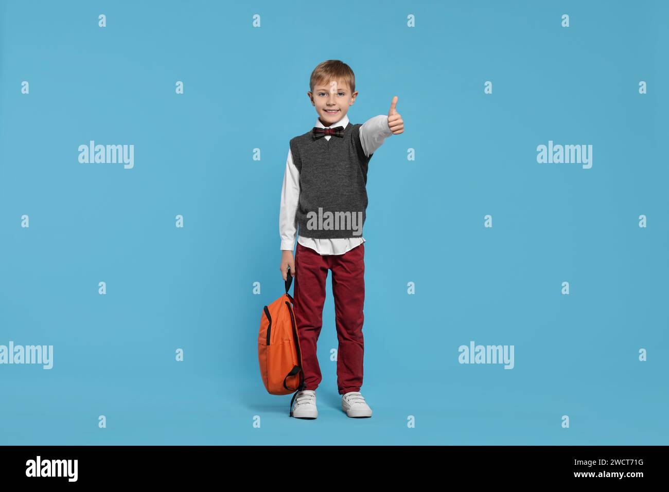 Happy schoolboy with backpack showing thumb up gesture on light blue ...