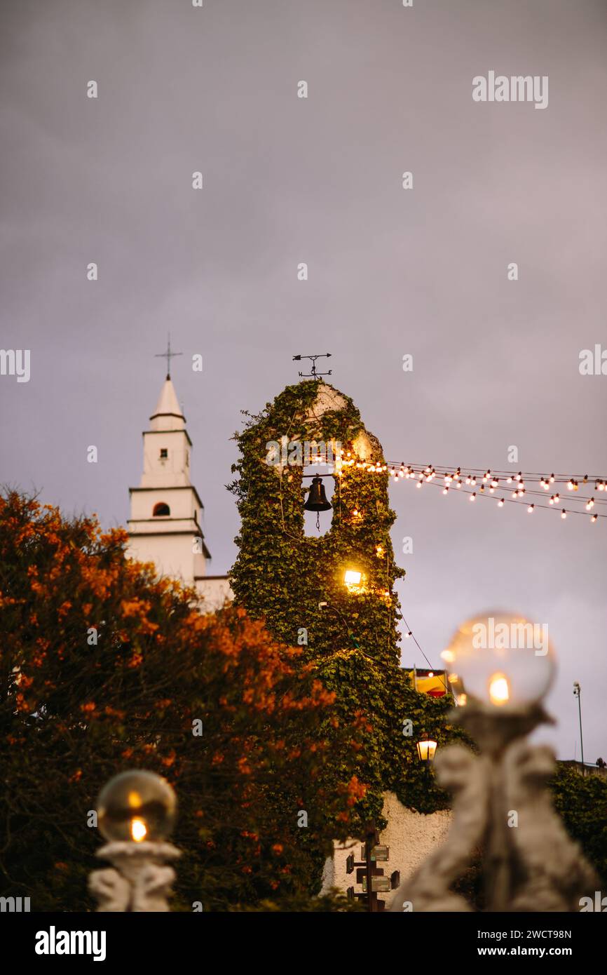 Twilight view of an ivy-covered church tower with lit lamps and garland lights against an evening sky Stock Photo