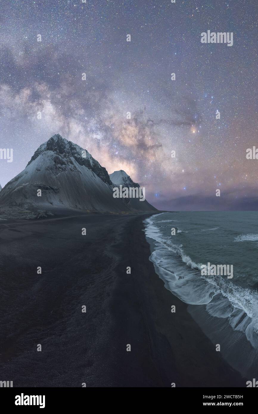 A towering mountain peak beside a black sand beach under the Milky Way ...