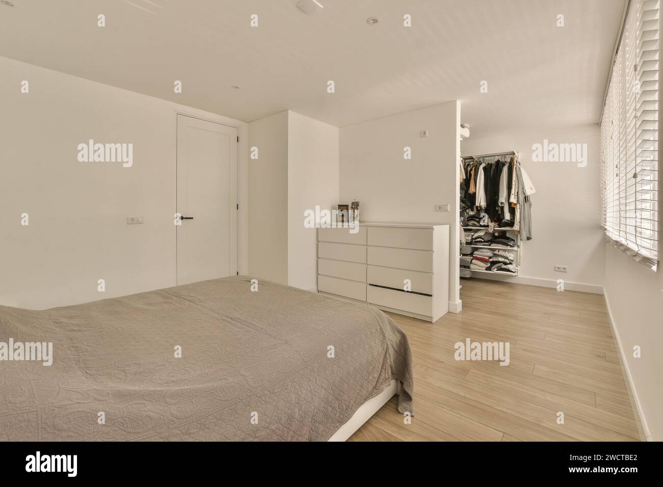 A welllit modern bedroom featuring a large bed, dresser, and a view