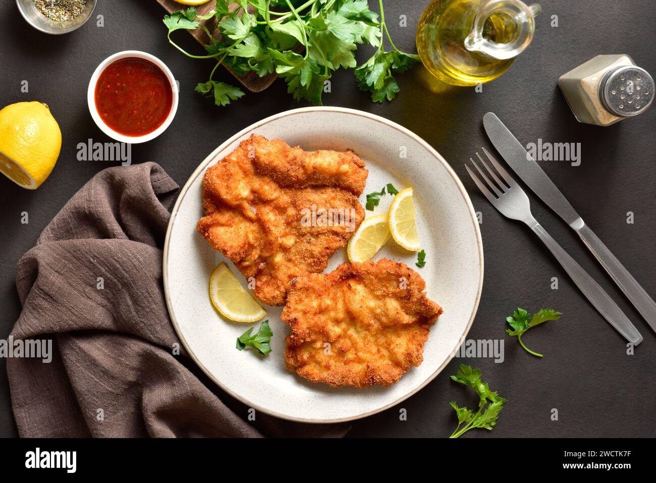 Schnitzel with lemon and leaves of parsley on white plate over brown stone background. Top view, flat lay Stock Photo