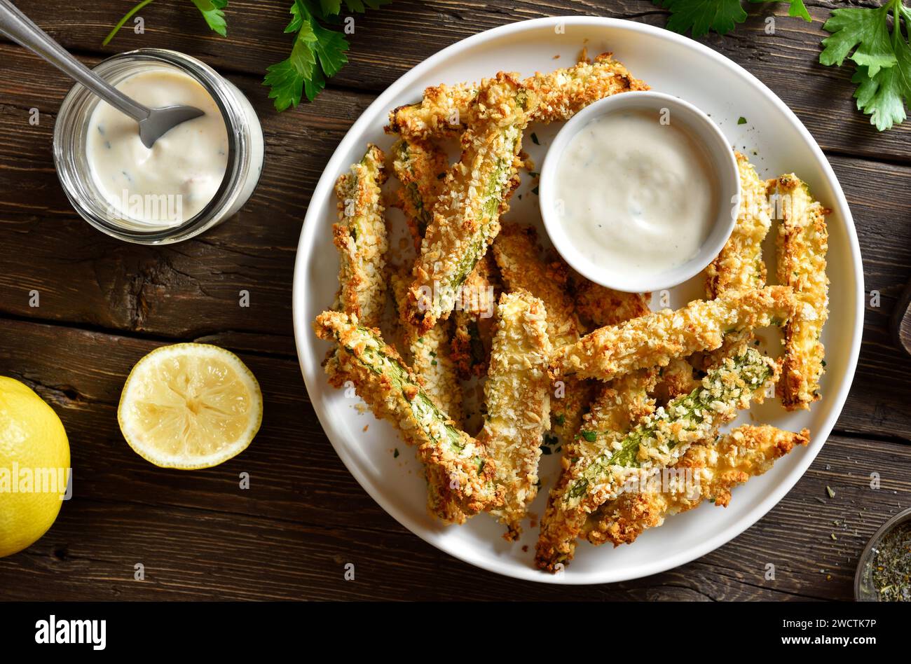Crunchy zucchini breaded sticks with dip sauce on plate over wooden background. Top view, flat lay Stock Photo