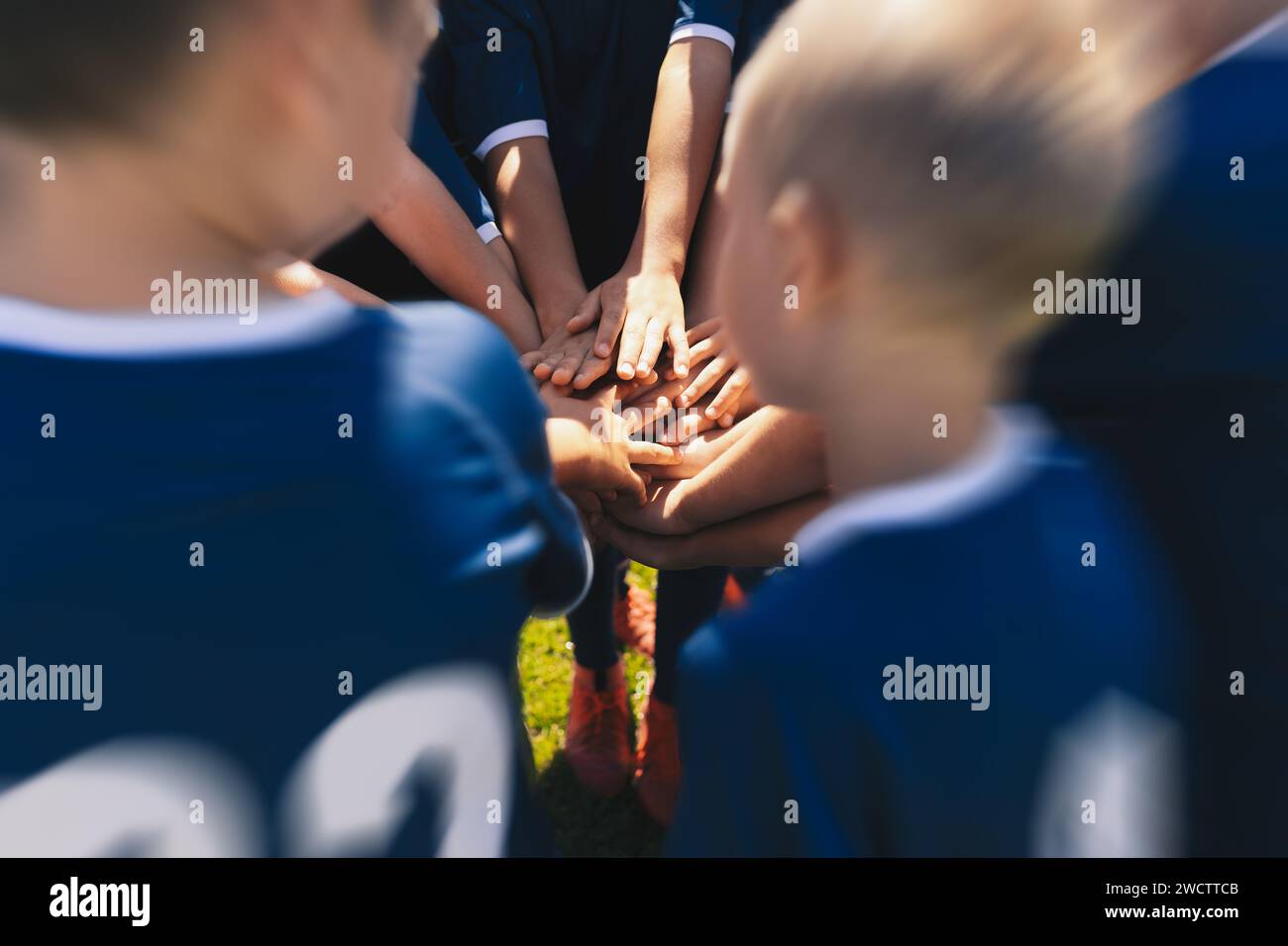 Happy Children Sports Team Stacking Hands. Kids Having Fun During Outdoor Physical Education Practice. Little Boys in Sports Clothes at Soccer Field Stock Photo