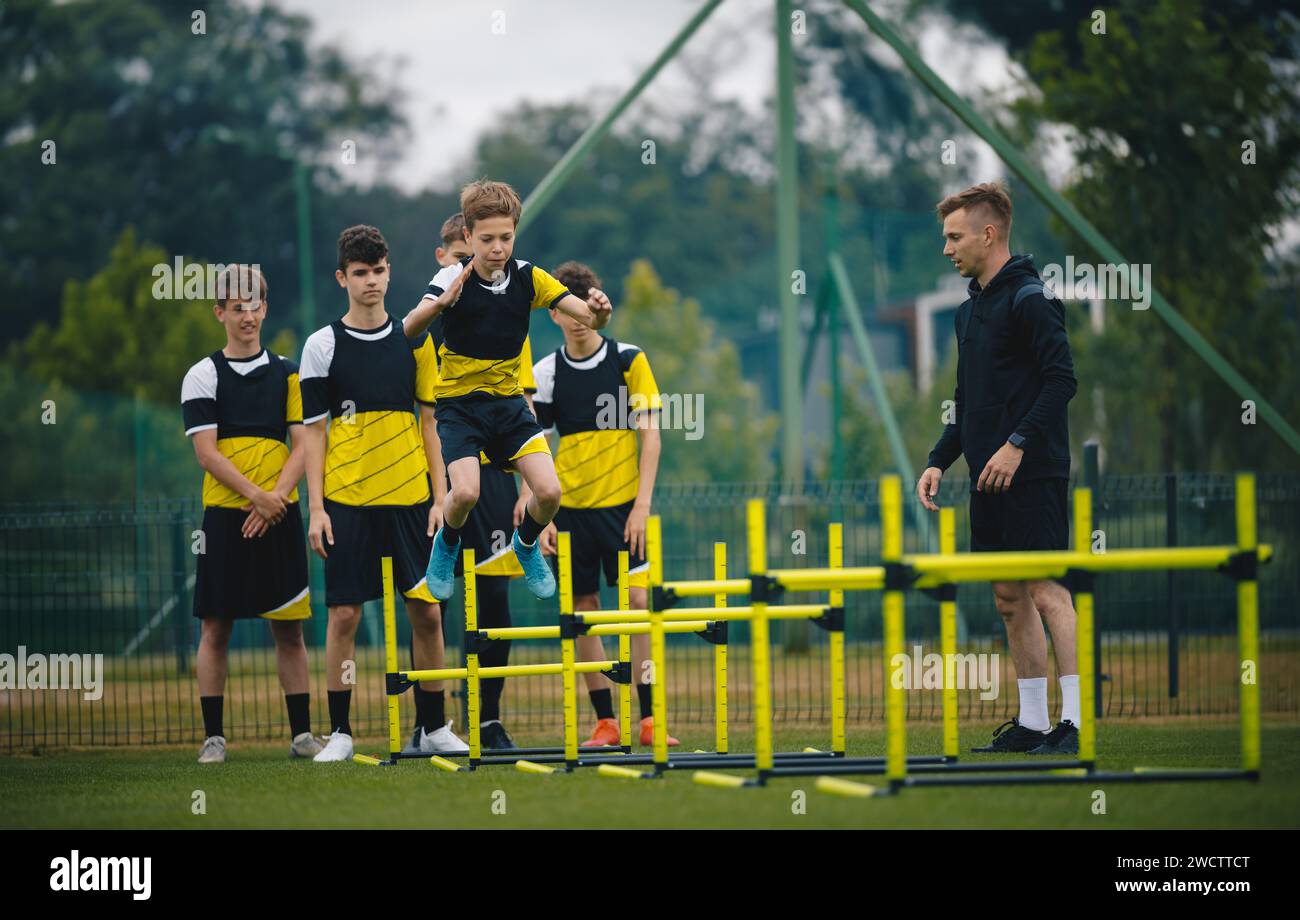 Teenagers on soccer training camp. Boys in football practice with a young coach. Junior-level athletes jump over hurdles and improve strength and coor Stock Photo