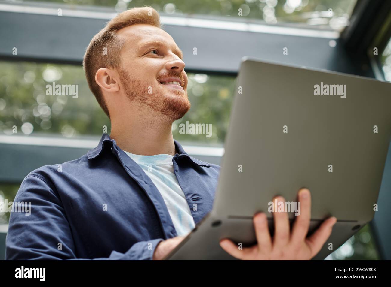 joyful good looking architect in everyday clothes holding his laptop and working on his startup Stock Photo