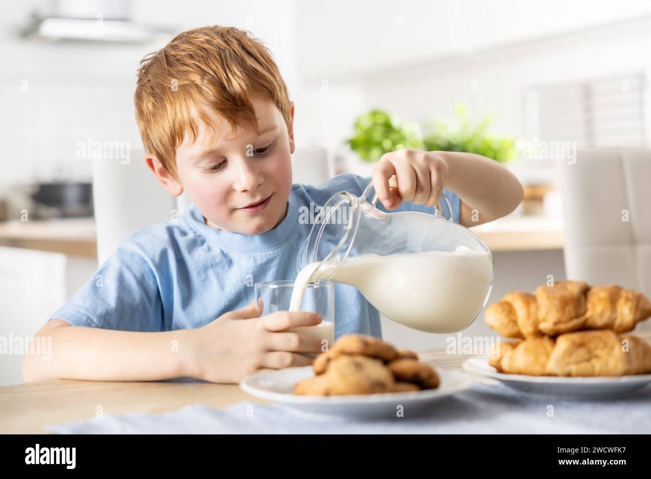 A little boy pours himself fresh milk during breakfast. Stock Photo