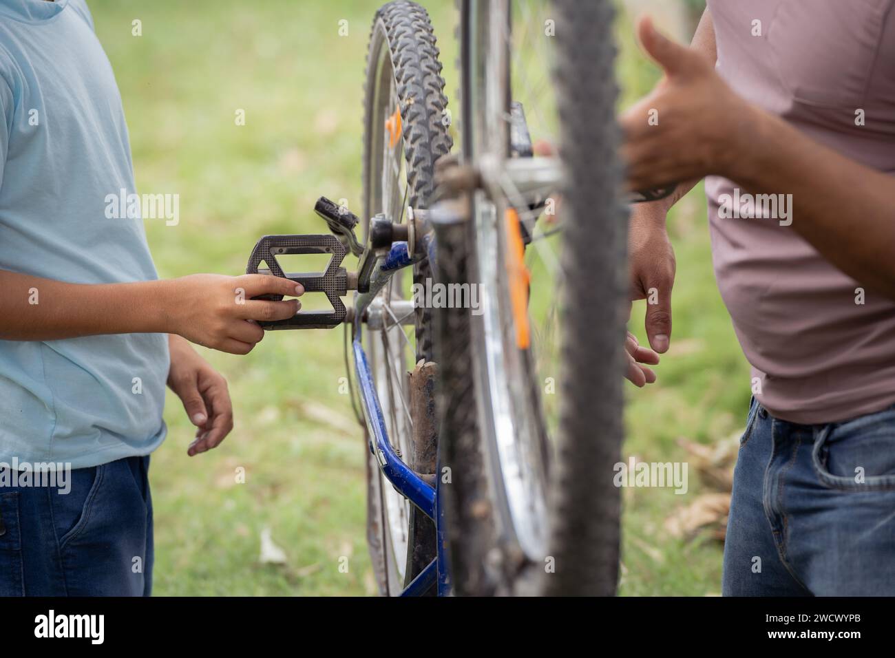 Close up shot of indian father with son repairing or checking bicycle at park during morning walk - concept of togetherness, maintenance and parents Stock Photo