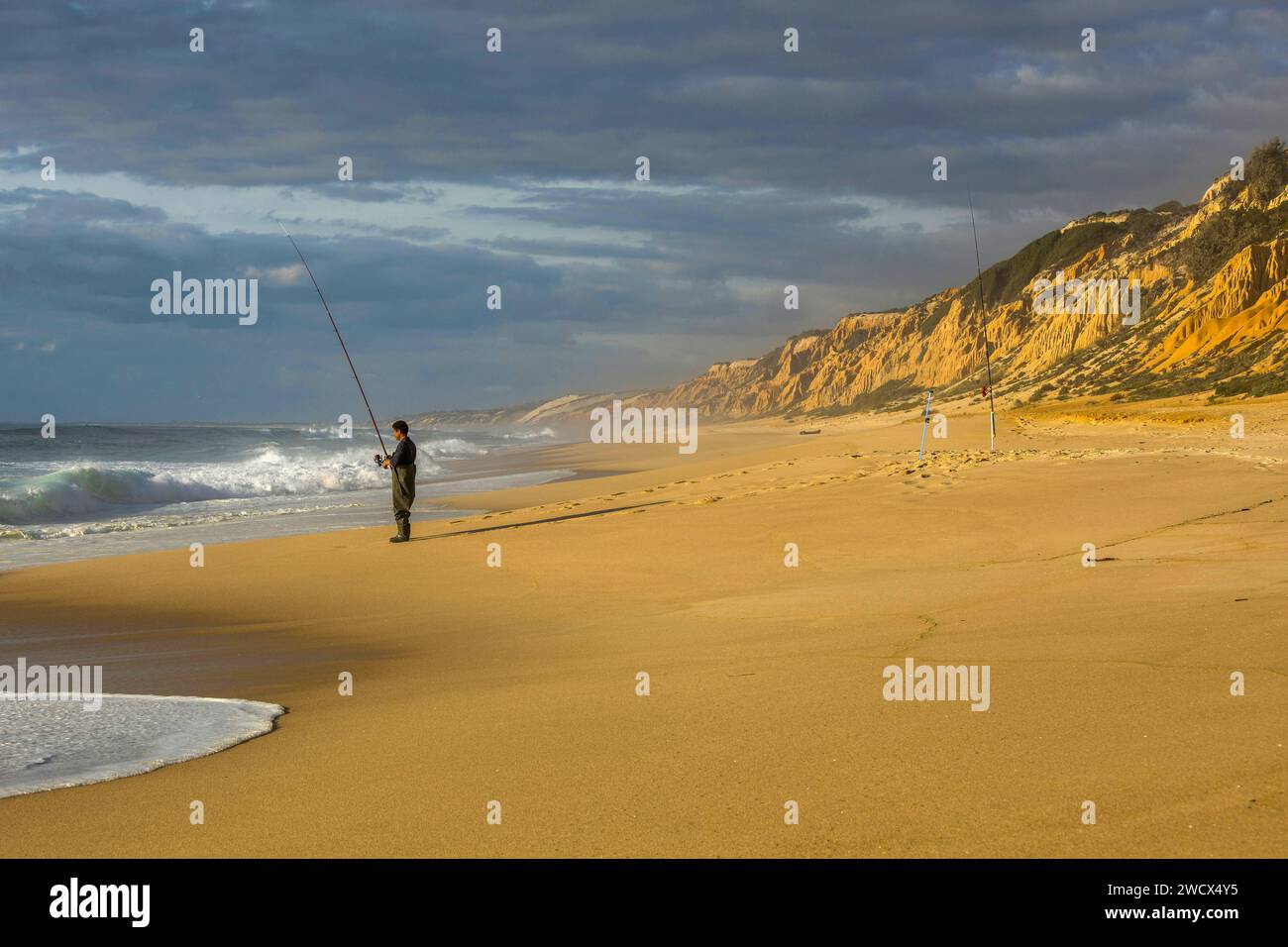 Portugal, Alentejo, Gale Fontainhas beach, fisherman casting fishing rod into the Atlantic Ocean on a beach flanked by ocher fossil cliffs five million years old Stock Photo