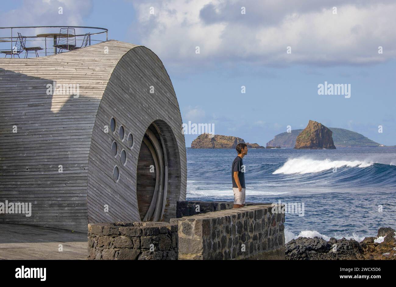 Portugal, Azores archipelago, Pico island, Madalena, man in front of the entrance to the cella bar, a sort of designer wooden bubble facing the ocean and the island of Faial Stock Photo