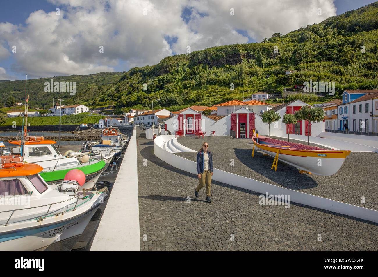 Portugal, Azores archipelago, Pico island, Lajes de Pico, young woman walking in front of an old whaling boat placed in front of white houses and the marina Stock Photo