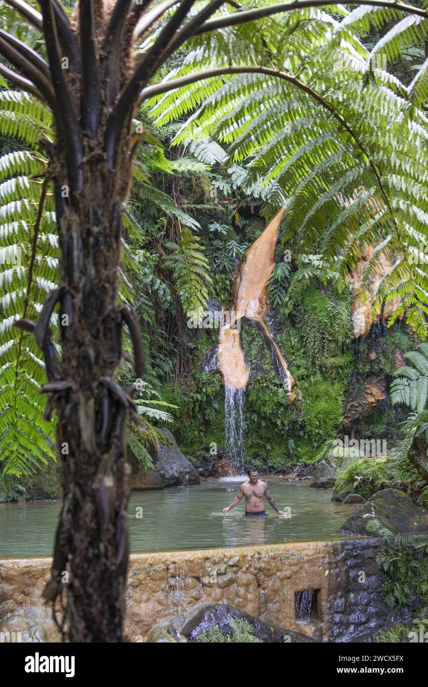 Portugal, Azores archipelago, Sao Miguel island, Caldera Velha, man bathing in a hot water pool under a waterfall surrounded by exuberant vegetation and tree ferns Stock Photo