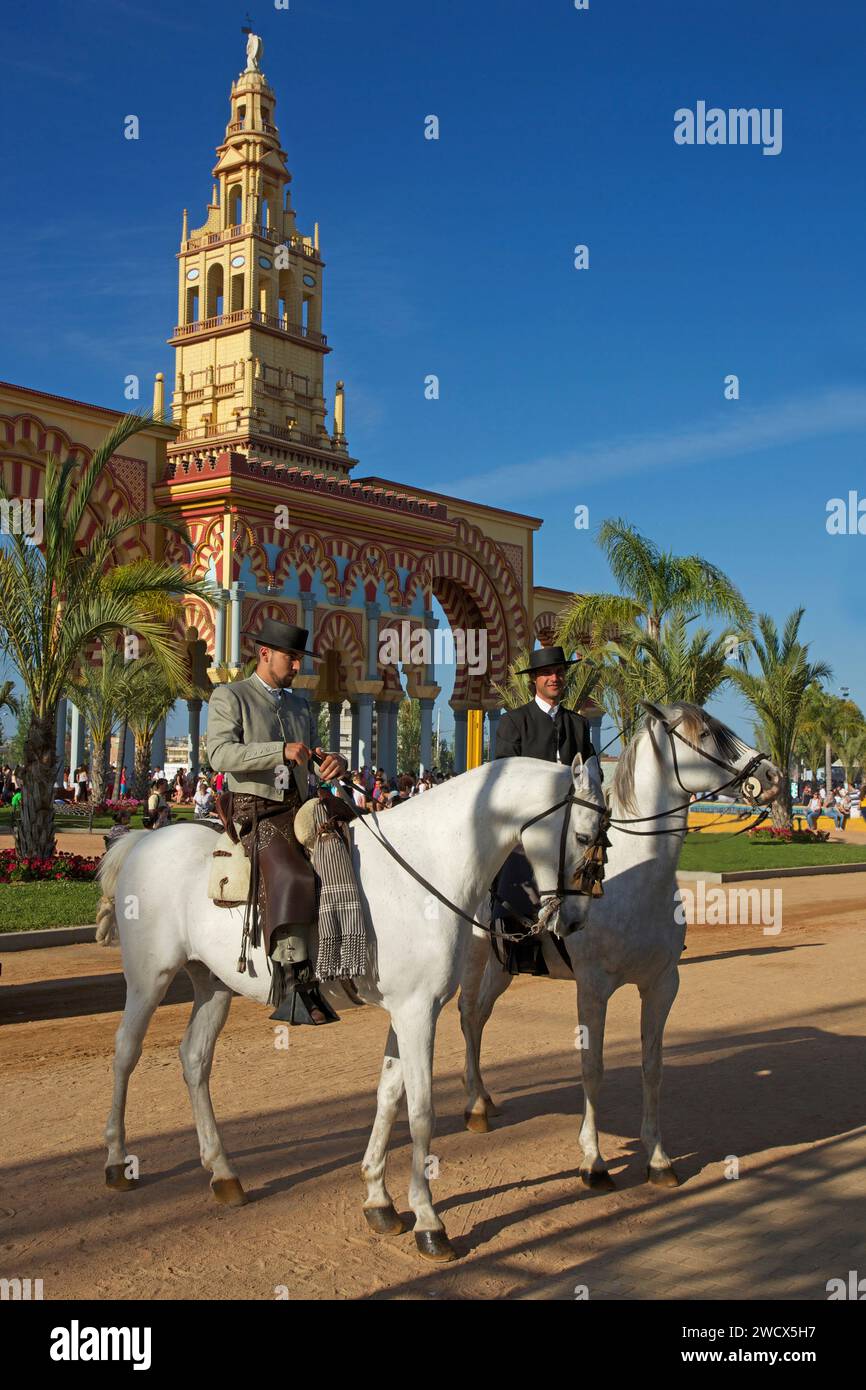 Spain, Andalusia, Cordoba, riders in traditional costume on horseback in front of the monumental yellow and red entrance gate of the feria de Nuestra señora de la salud Stock Photo