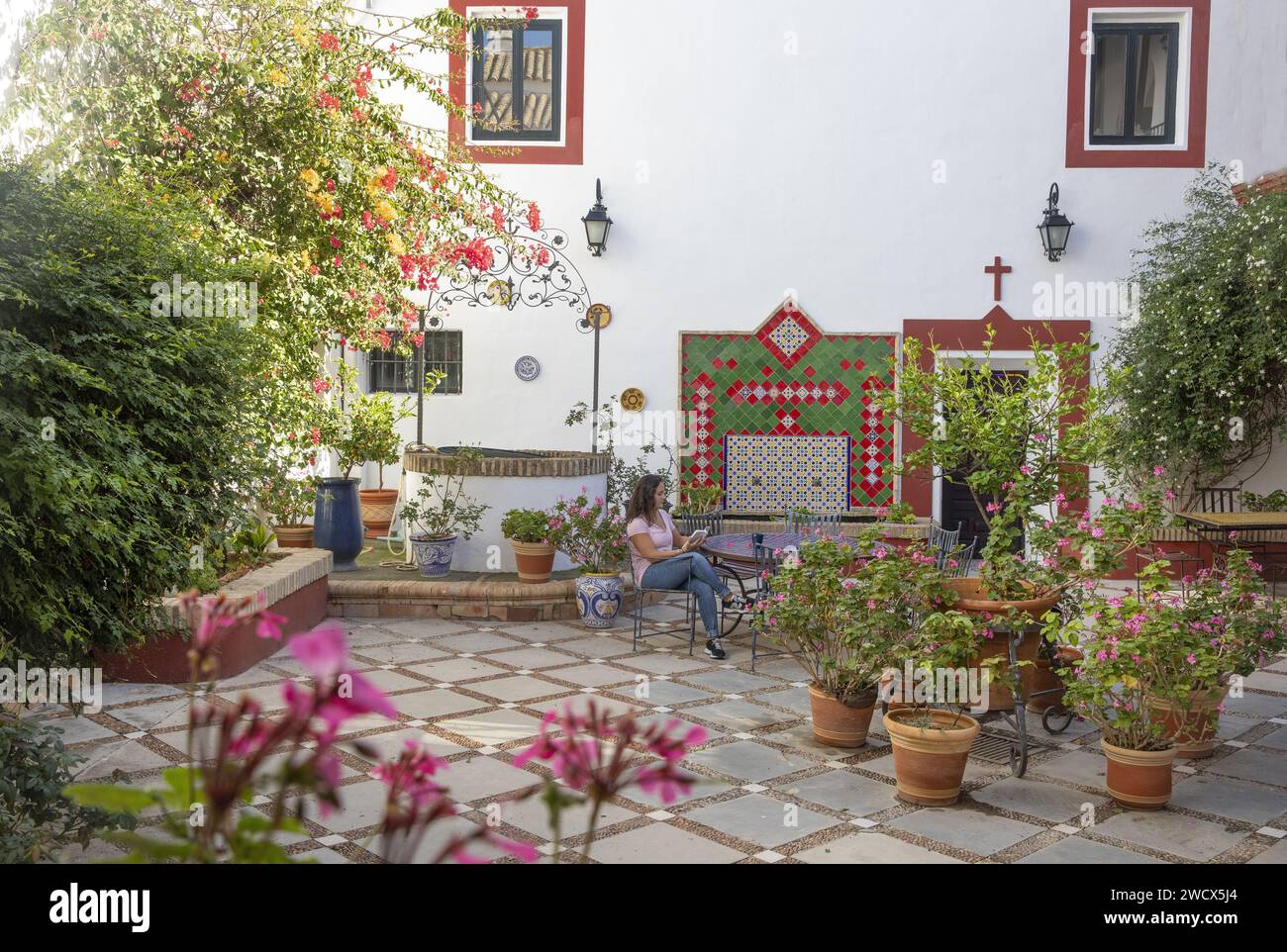 Spain, Andalusia, Moron de la Frontera, hacienda las Alcabalas, woman reading at a zellige table in the flowered patio decorated with azulejos of an Andalusian Sevillian-style hacienda Stock Photo