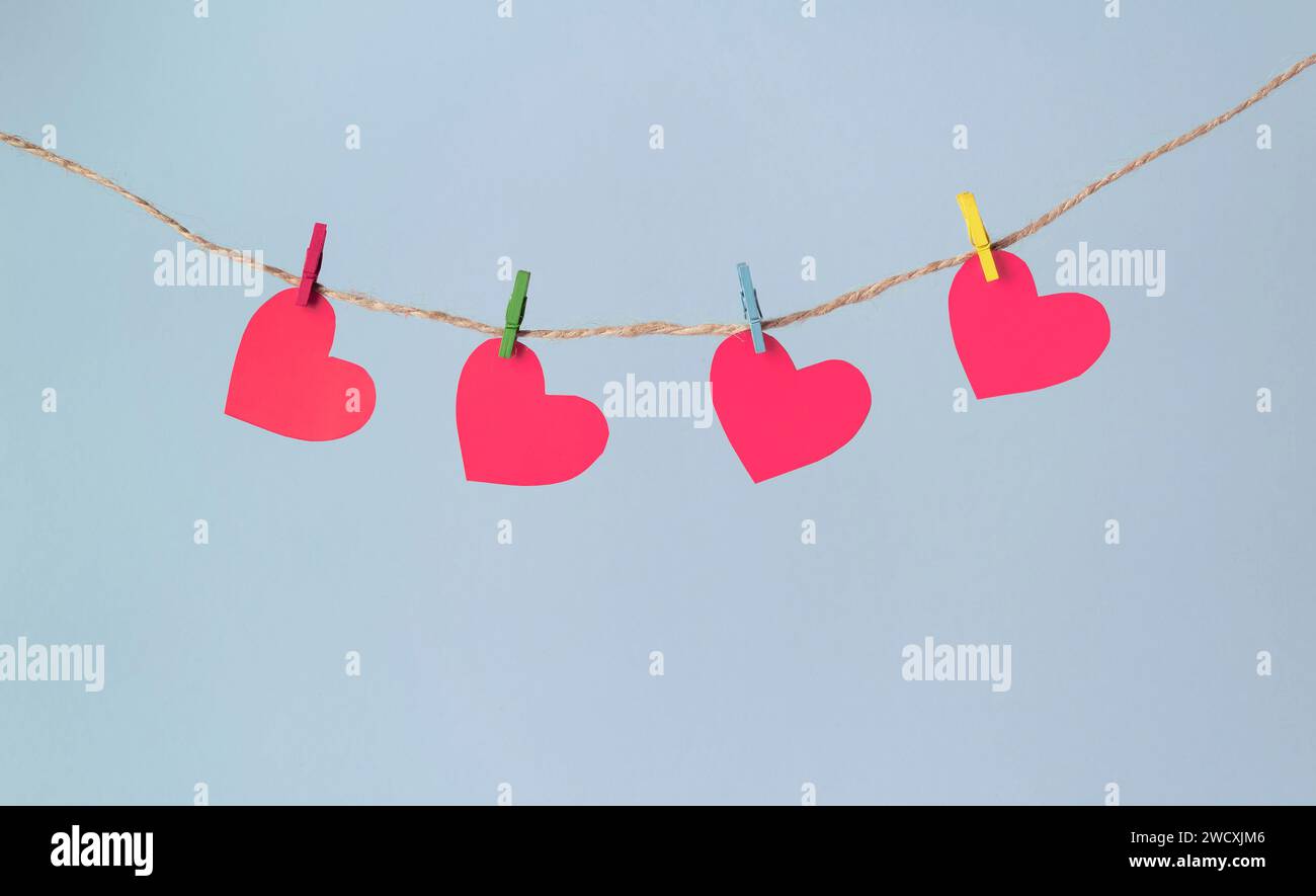 Paper hearts hang on clothespins on a rope on a pastel blue background. Valentine's day concept. Stock Photo