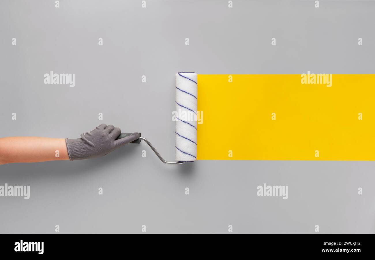 Girl in a glove paints a yellow strip with a roller on a gray wall. Creative renovation concept. Stock Photo