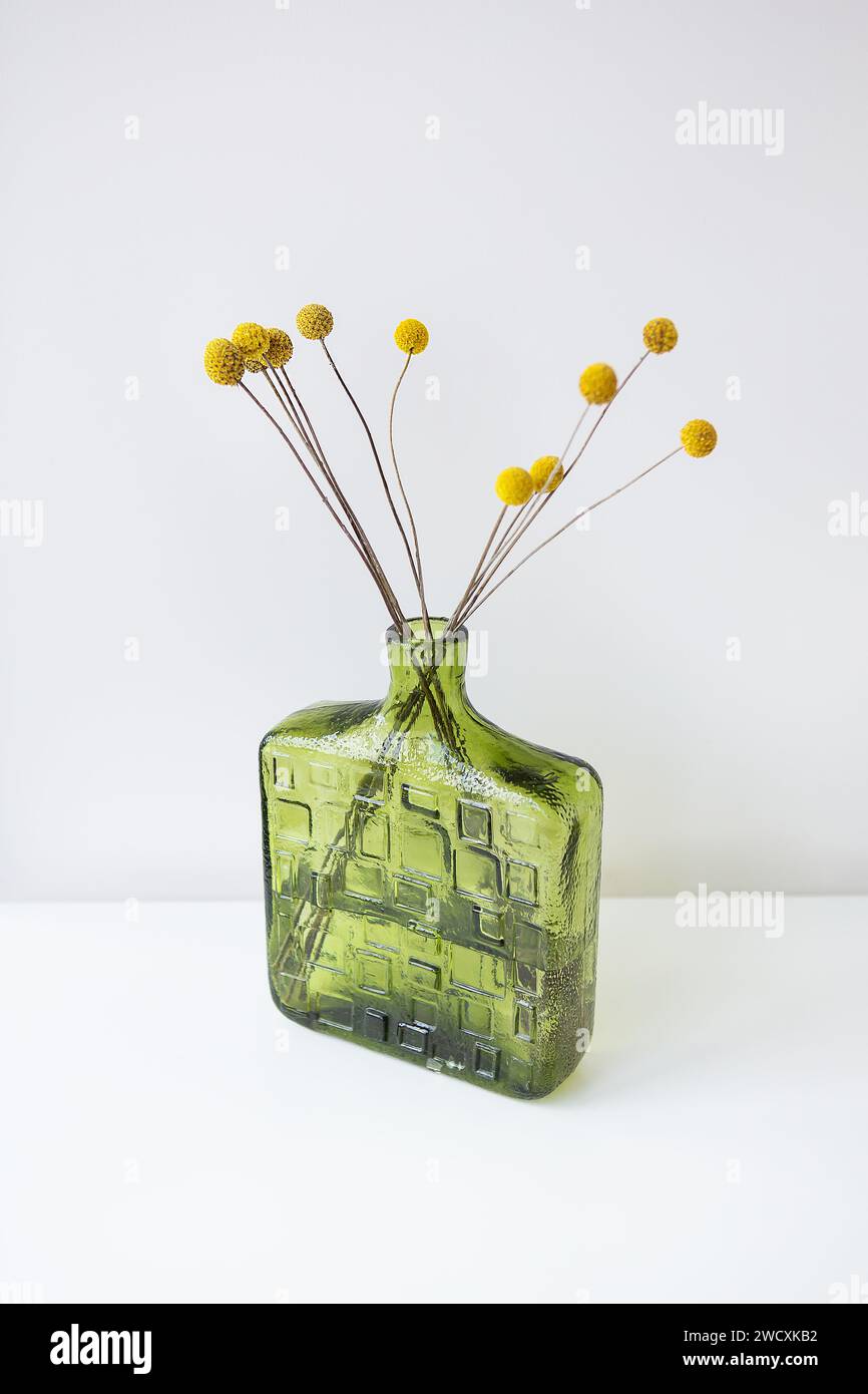 A green textured glass vase with yellow Craspedia flowers against a white background. Simple and elegant Stock Photo