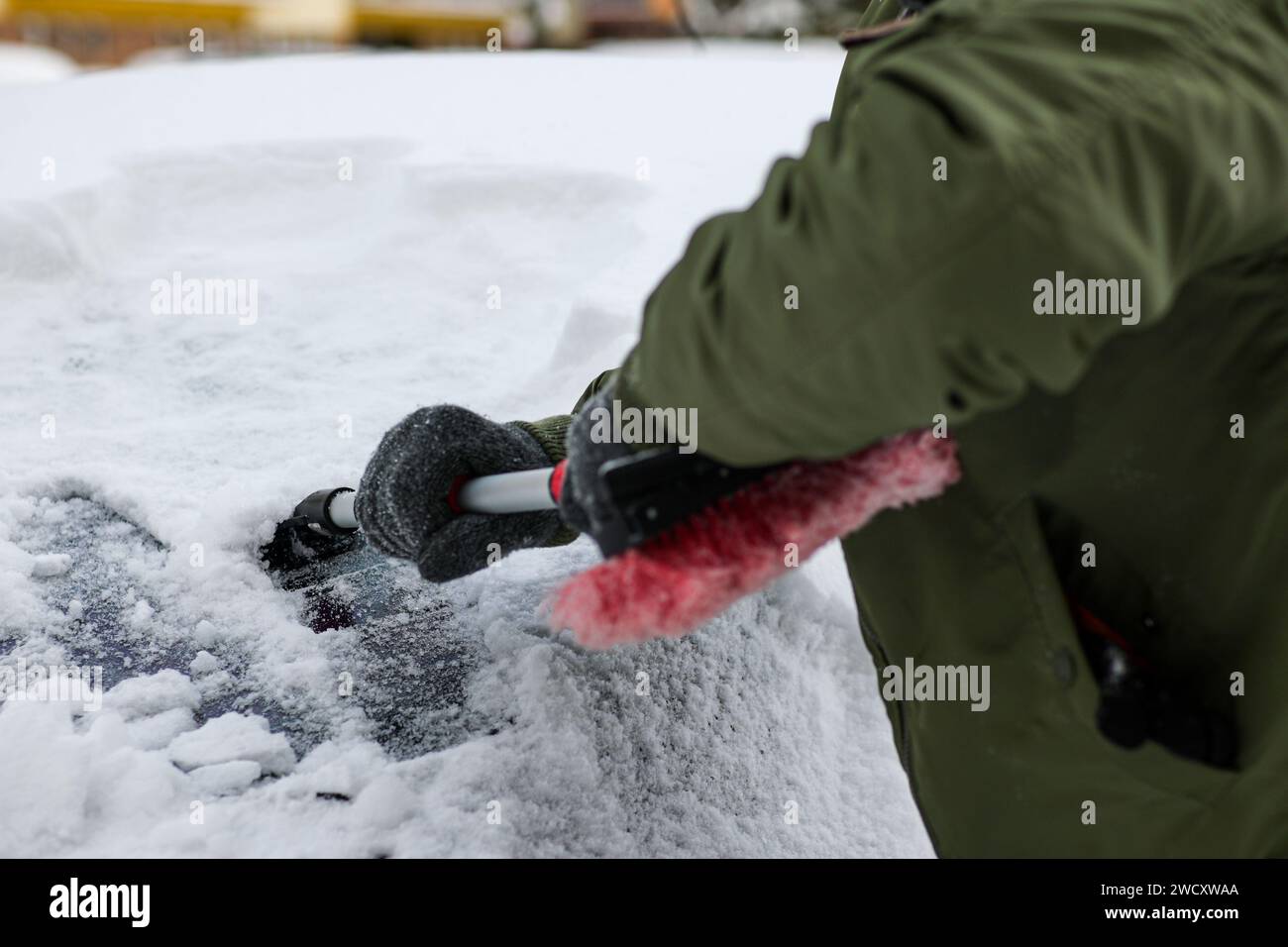 guy in jacket, hat and gloves scrapes car windows from ice to blizzard ...