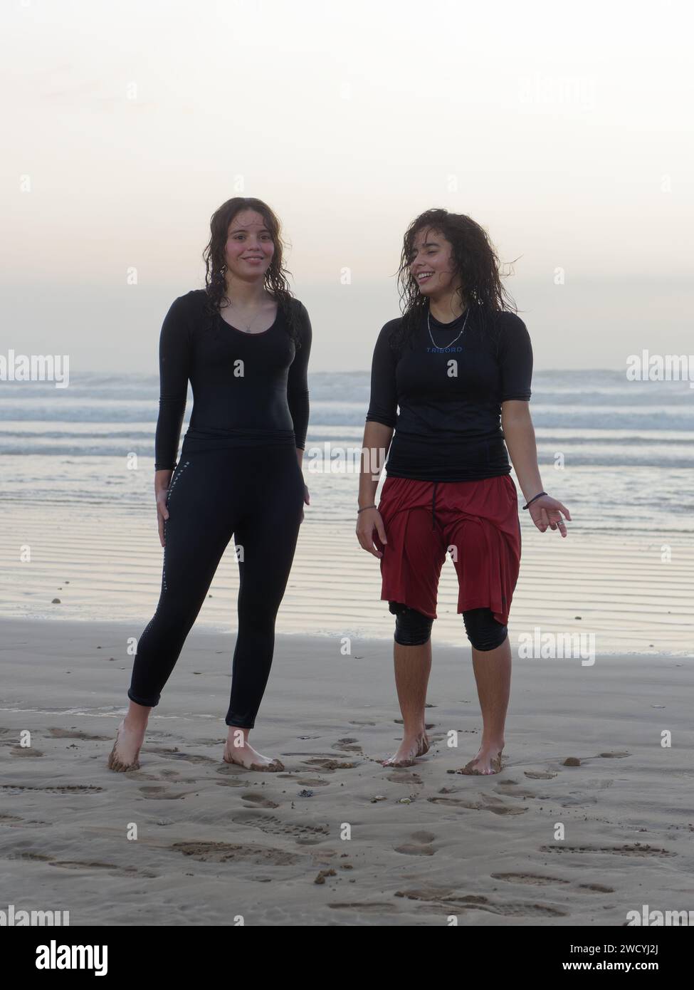 Two young women in bathing costumes and wet hair stand on the beach after a sunset dip in the sea in Essaouira, Morocco, Jan 17th 2024 Stock Photo