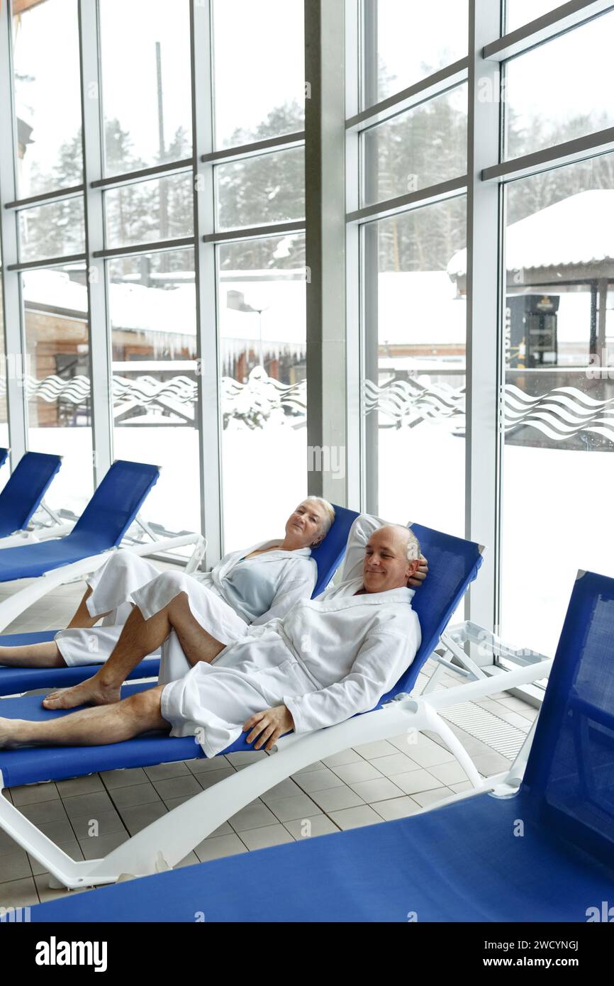 An elderly woman with a man in bathrobes on a sun lounger by the pool