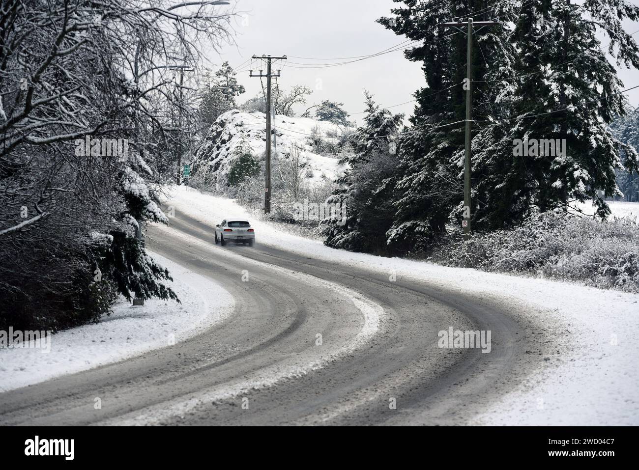 A car drives down a snow covered road on Vancouver Island, British Columbia, Canada following a winter storm Stock Photo