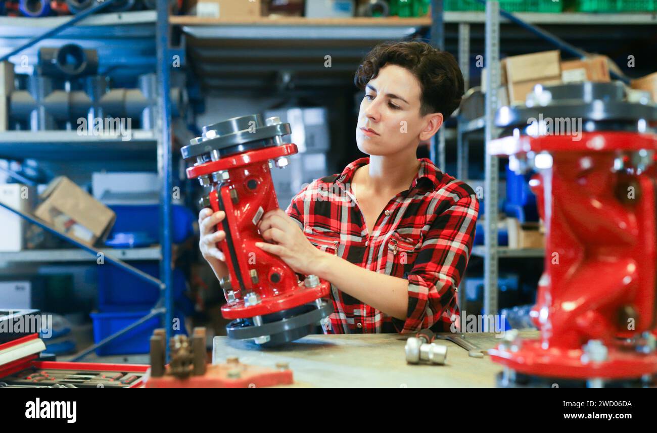 Female worker assembles shutoff valves using various tools in factory indoor Stock Photo