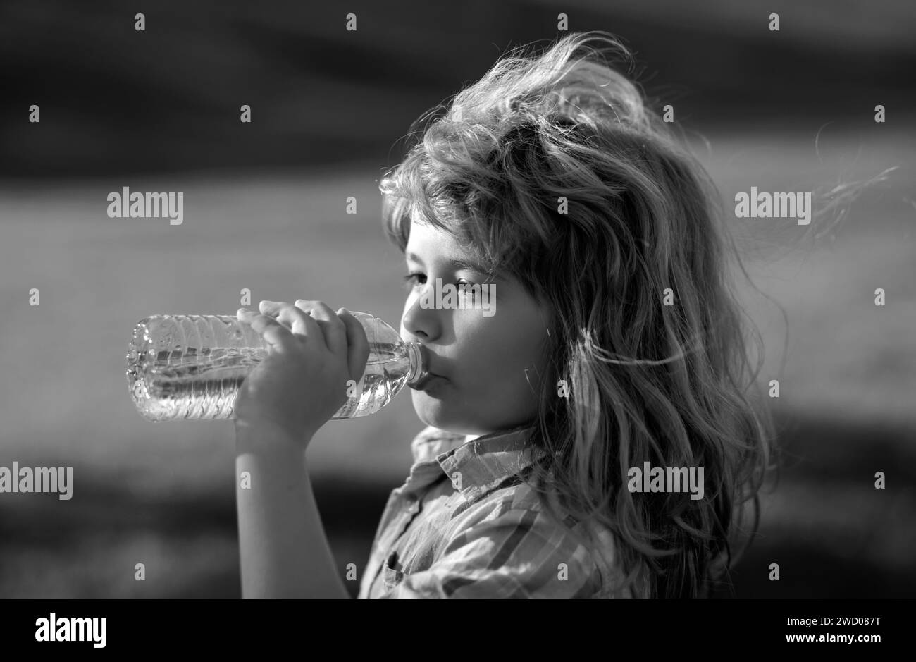 Child drinking water from pet bottle outdoor in park. Kid drinking. Boy drinking water in the park, holding plastic bottle. Thirsty child. Stock Photo