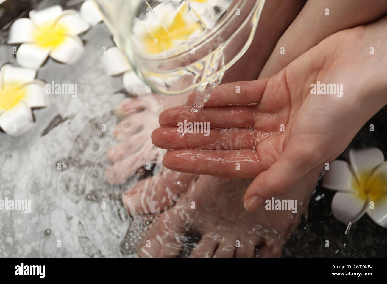 Woman pouring water onto hand while soaking her feet in bowl, above