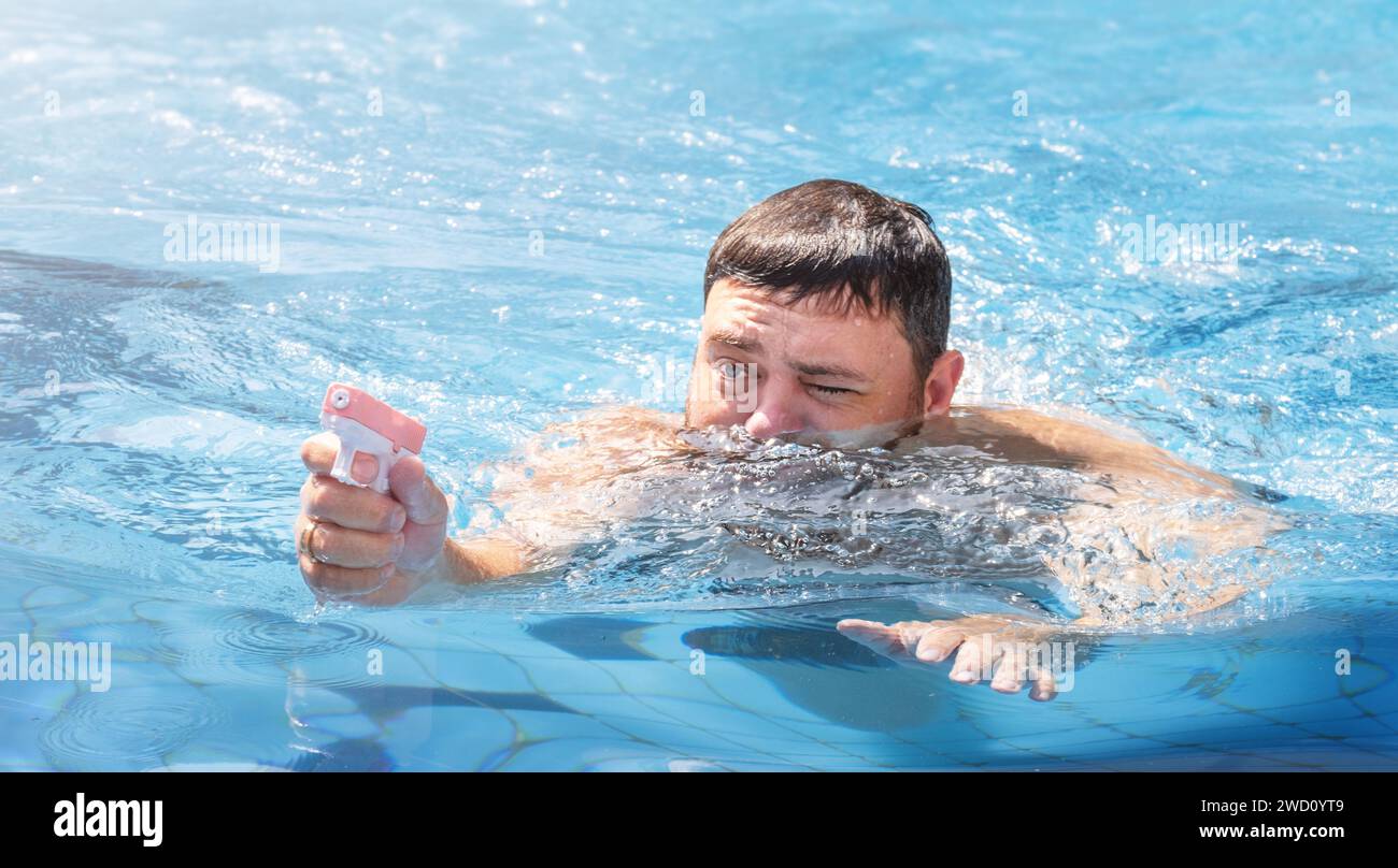 Man playing with water gun in swimming pool on vacation Stock Photo