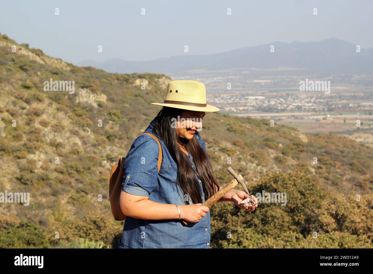 Latin adult woman geologist studies the details and characteristics of rocks, minerals and fossils in the mountain Stock Photo