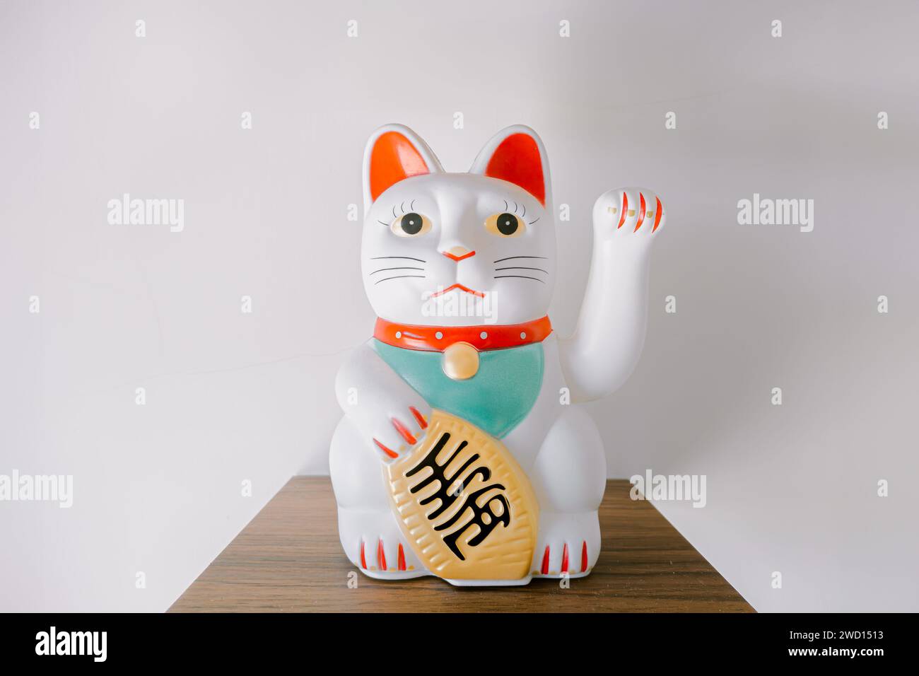 White Chinese Lucky Cat waving statue on the wooden shelf on the white background Stock Photo
