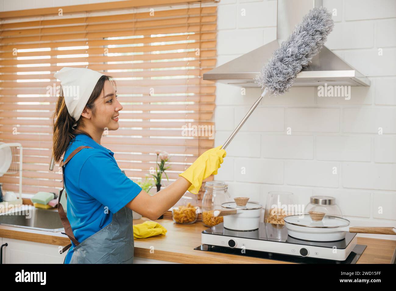 Maid in workwear and gloves cleans home dusts kitchen ventilation. Emphasizing modern housework Stock Photo