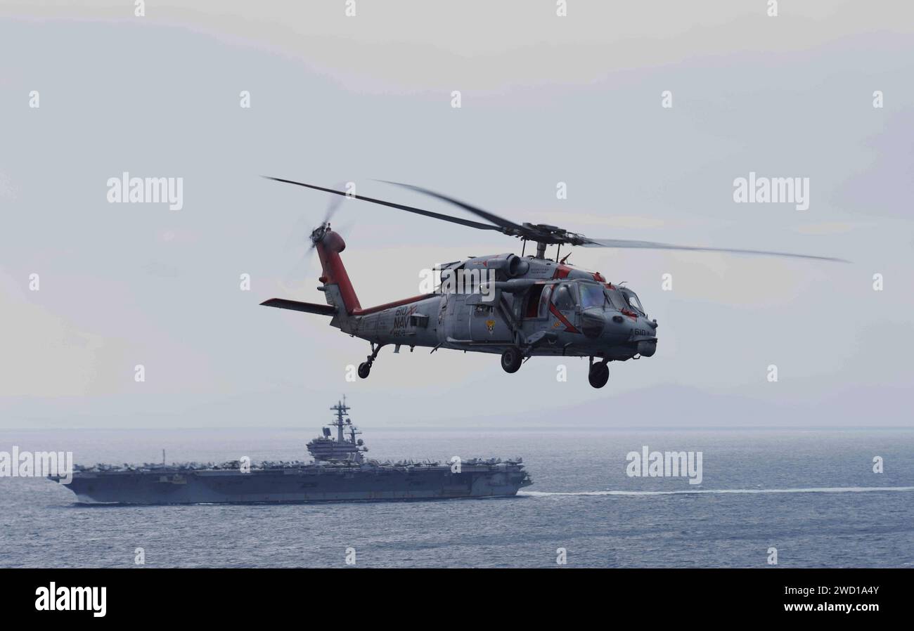 An MH-60S Sea Hawk helicopter monitors the aircraft carrier USS George H.W. Bush. Stock Photo