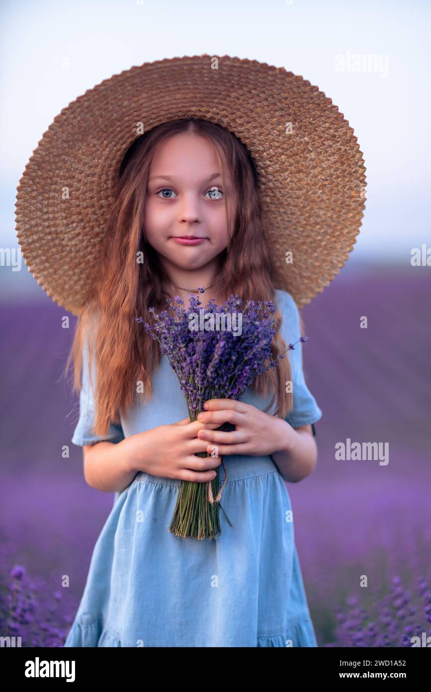 Girl lavender field in a blue dress with flowing hair in a hat stands ...